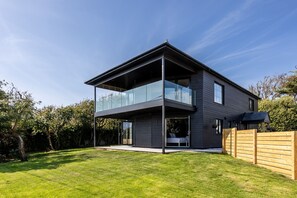 A modern two-story house with a balcony, a wooden fence, and a well-maintained lawn.