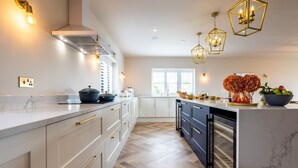 A modern kitchen with white cabinetry, a marble countertop, and a built-in oven. - Bluebells: Eco-Friendly 4-Bed Home with Sea Views in Llanfaelog | Managed by Anglesey Holiday Lettin (Llanfaelog)