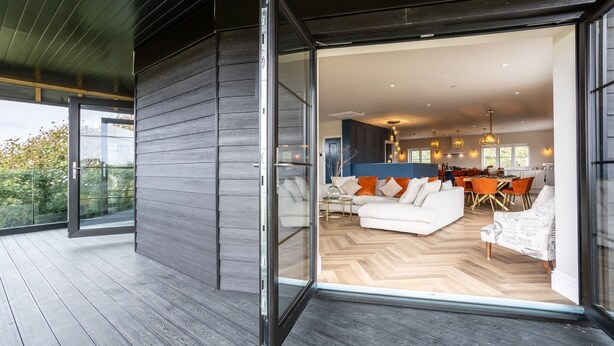 A modern interior with a sliding glass door leading to a living area with a sofa, dining table, and chairs. - Bluebells: Eco-Friendly 4-Bed Home with Sea Views in Llanfaelog | Managed by Anglesey Holiday Lettin (Llanfaelog)