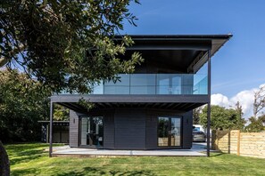 Un edificio moderno de dos plantas con techo plano, amplios ventanales y fachada oscura.