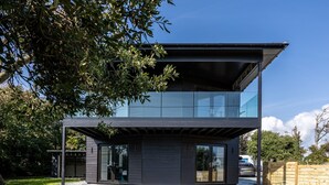A modern two-story house with a flat roof, large glass windows, and a dark exterior. - Bluebells: Eco-Friendly 4-Bed Home with Sea Views in Llanfaelog | Managed by Anglesey Holiday Lettin (Llanfaelog)