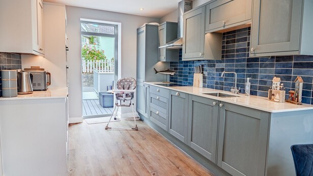 A modern kitchen with grey cabinets, a blue tiled backsplash, and a wooden floor.