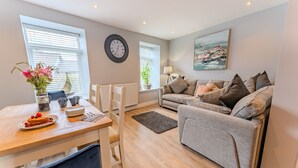 A modern living room with a wooden dining table set for breakfast, a grey sofa, and a painting on the wall.