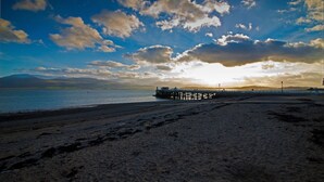 A beach with a pier extending into calm waters, under a partly cloudy sky.