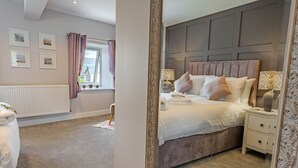 A well-lit bedroom with a large bed, bedside tables, a mirror, and framed pictures on the wall.