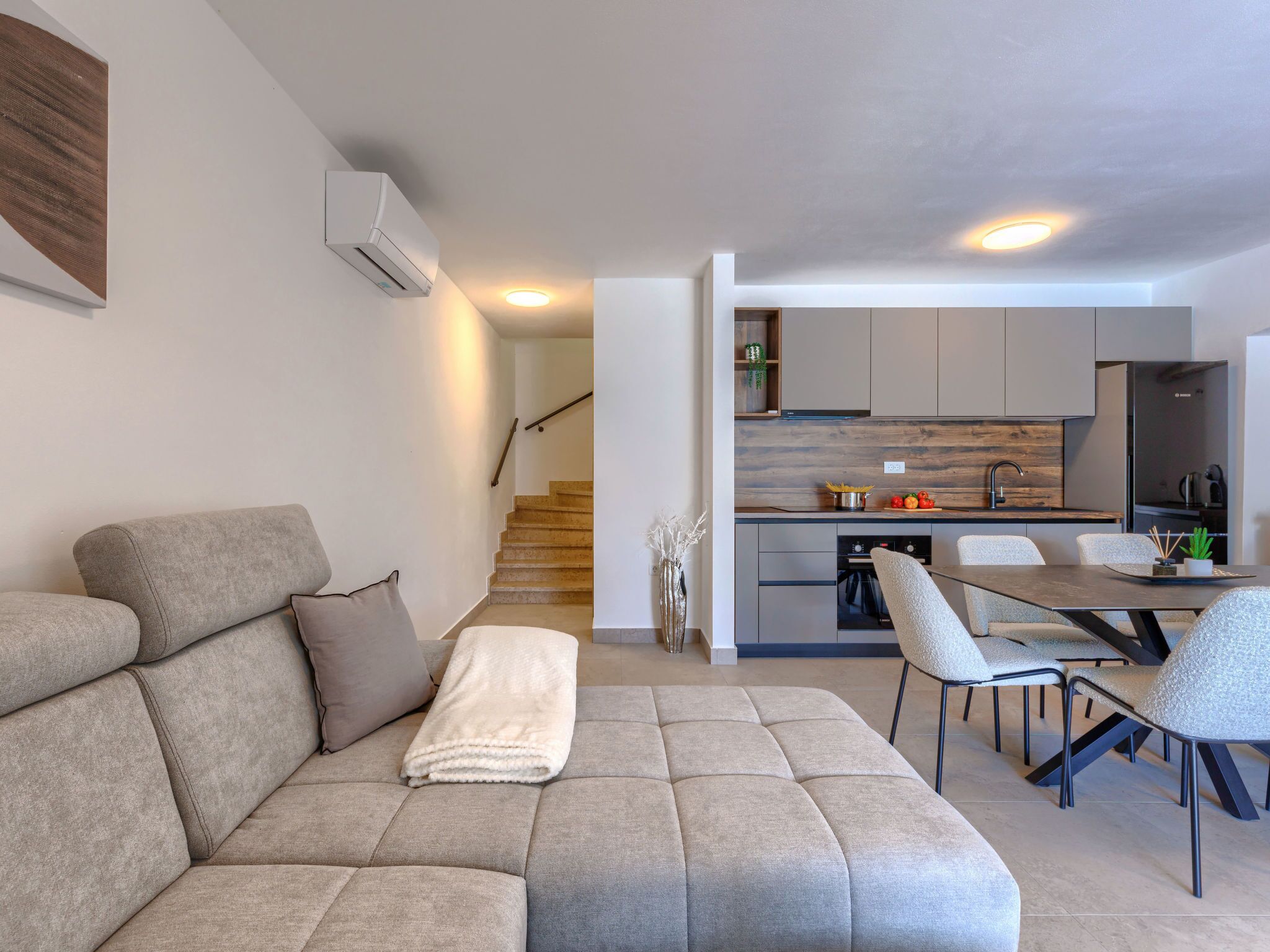 A modern living room with a sofa, a dining area with chairs, and a kitchen in the background.