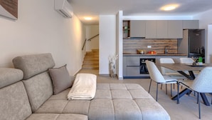 Un salon moderne avec un canapé, un coin repas avec des chaises et une cuisine en arrière-plan.