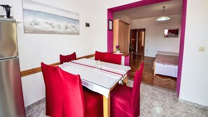 A dining area with a table set for four, red chairs, a refrigerator, and a painting on the wall. - Apartment Dajak by Interhome (Omiš)