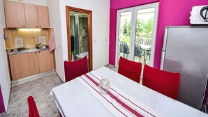 A compact kitchen with a built-in stove, a sink, and a microwave. There is a dining area with a table and chairs, and a sliding glass door leading to an outdoor patio with chairs and a table. - Apartment Dajak by Interhome (Omiš)