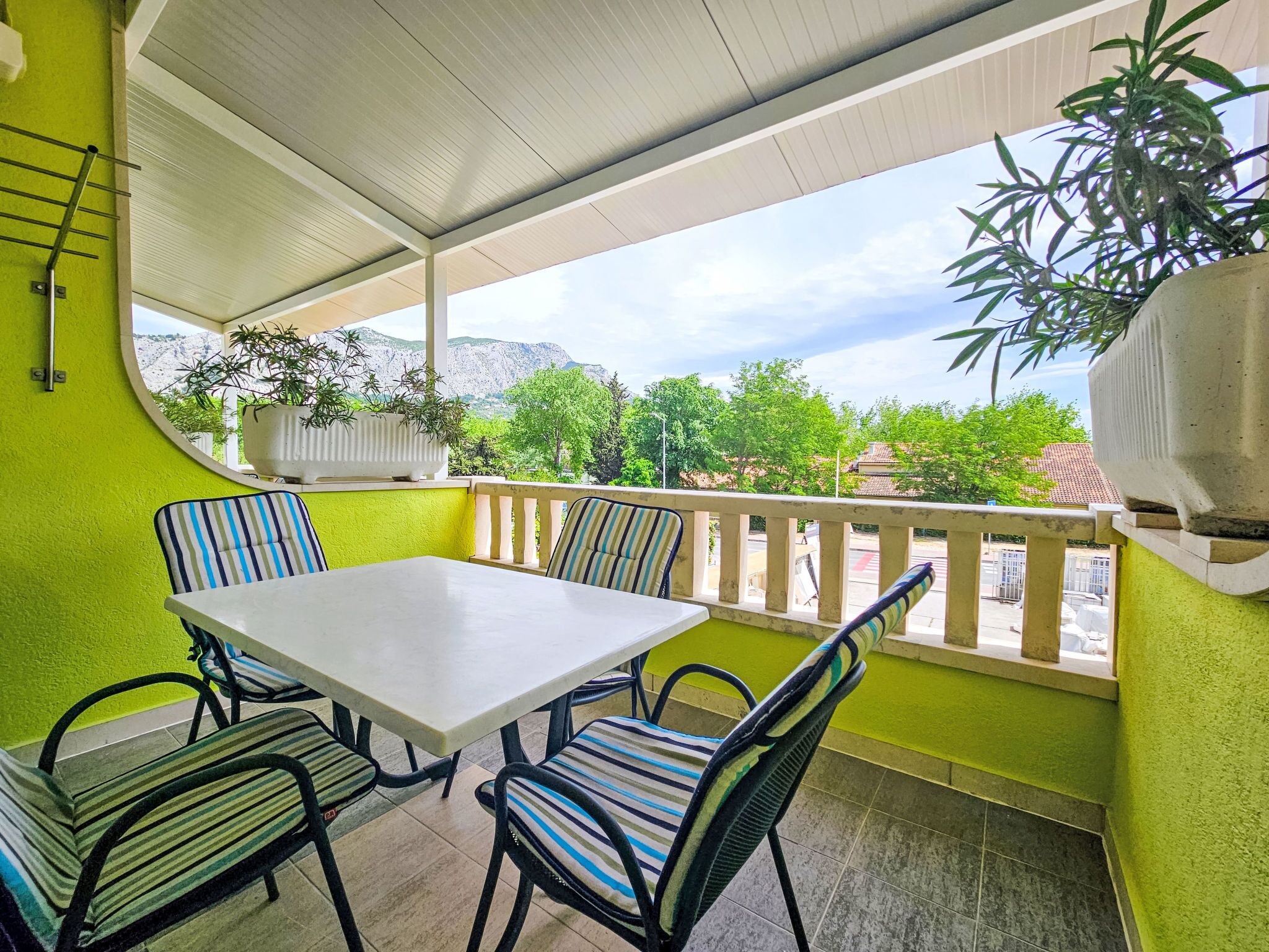 A covered patio with a table and chairs, a potted plant, and a view of greenery and mountains.