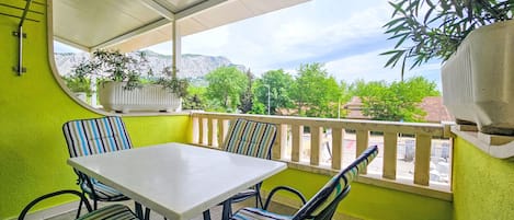 Eine überdachte Terrasse mit Tisch und Stühlen, einem Topfpflanzen und Blick auf Grünflächen und Berge.