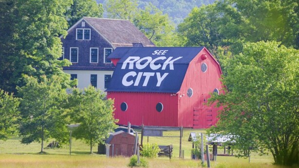 A red barn with a sign that reads "SEE ROCK CITY" in front of a house.