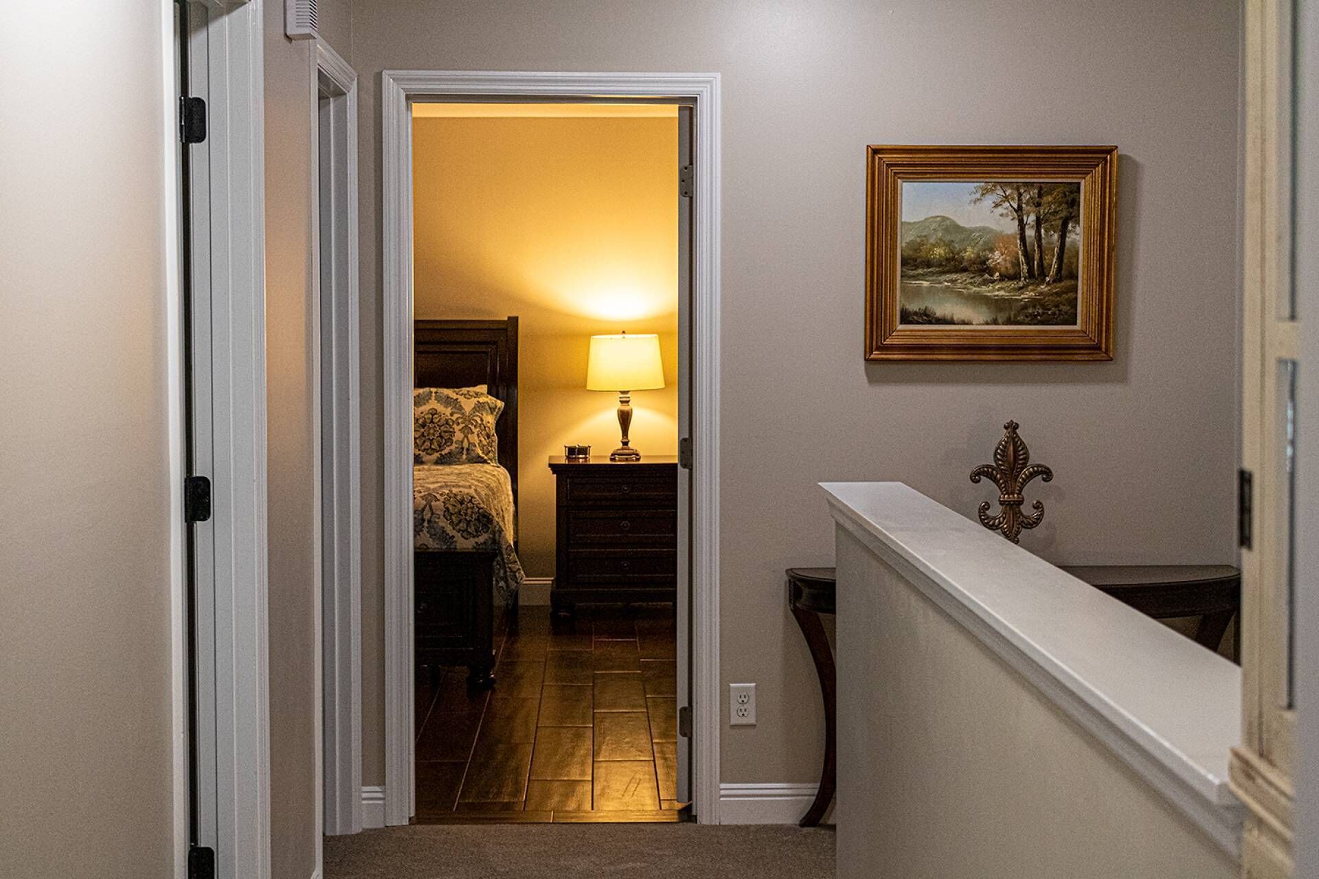 A hallway with a bed, a nightstand, a lamp, and a painting on the wall.