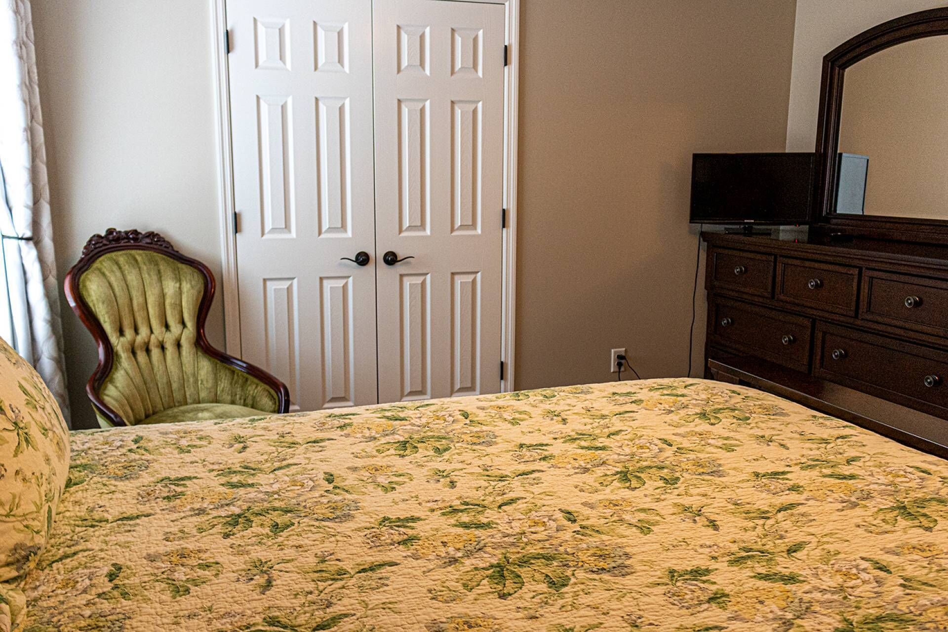 A bedroom with a bed, a dresser, a chair, and a television.