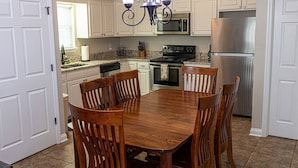A kitchen with white cabinets, a stainless steel refrigerator, a black stove, and a dining table with wooden chairs.