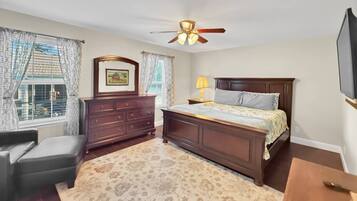 A bedroom with a bed, a dresser, a chair, a ceiling fan, and a TV.