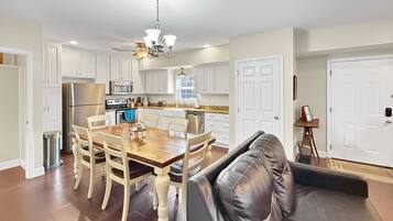 A modern kitchen with white cabinetry, a dining table with chairs, a black leather sofa, and a chandelier.
