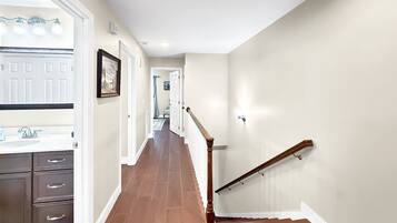 A hallway with a wooden staircase, a white door, and a bathroom with a sink and cabinets.
