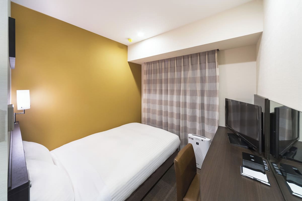 Habitación de hotel con cama, escritorio, televisor de pantalla plana, una mesita y ventana con cortinas.