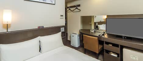 A hotel room with a bed, a desk with a flat-screen TV, a mirror, a hairdryer, and a small refrigerator.