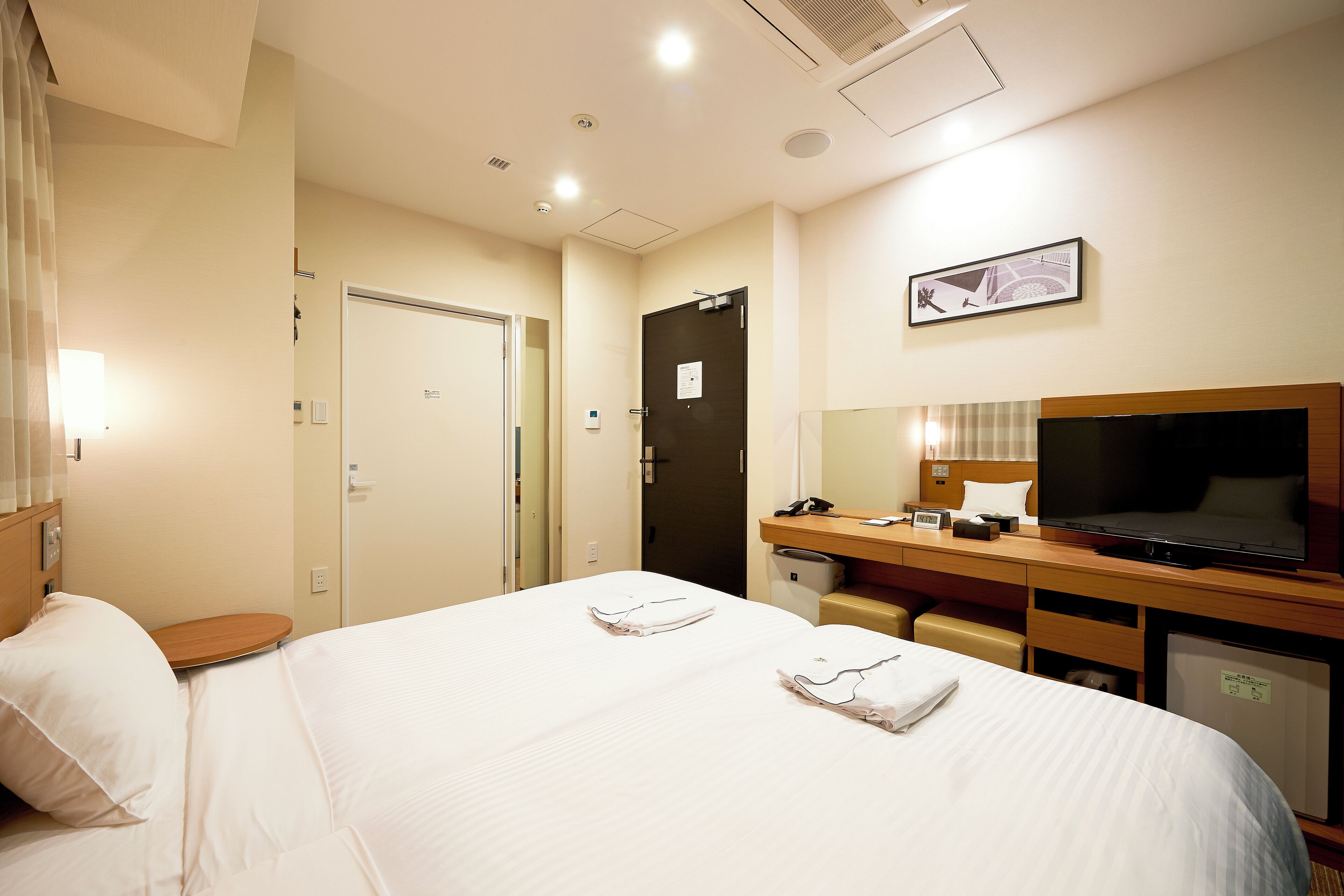 A hotel room with a bed, a desk with a television, a mirror, and a door.