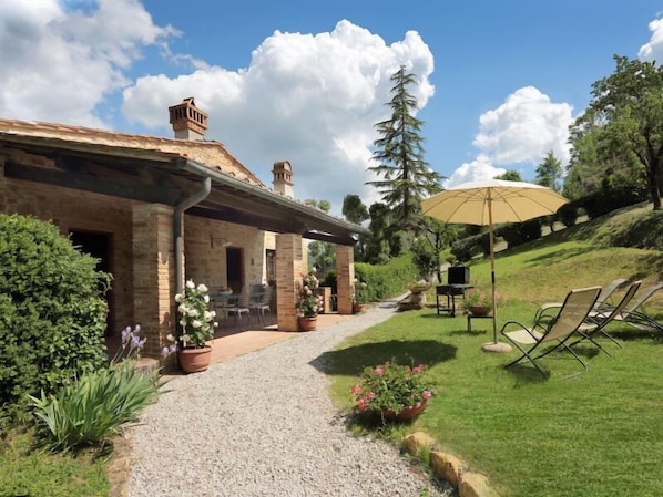 A stone building with a covered patio, outdoor seating, and a grassy area with a large umbrella. - POMARIUM - Main residence ground floor 135 m2 (Montaione)