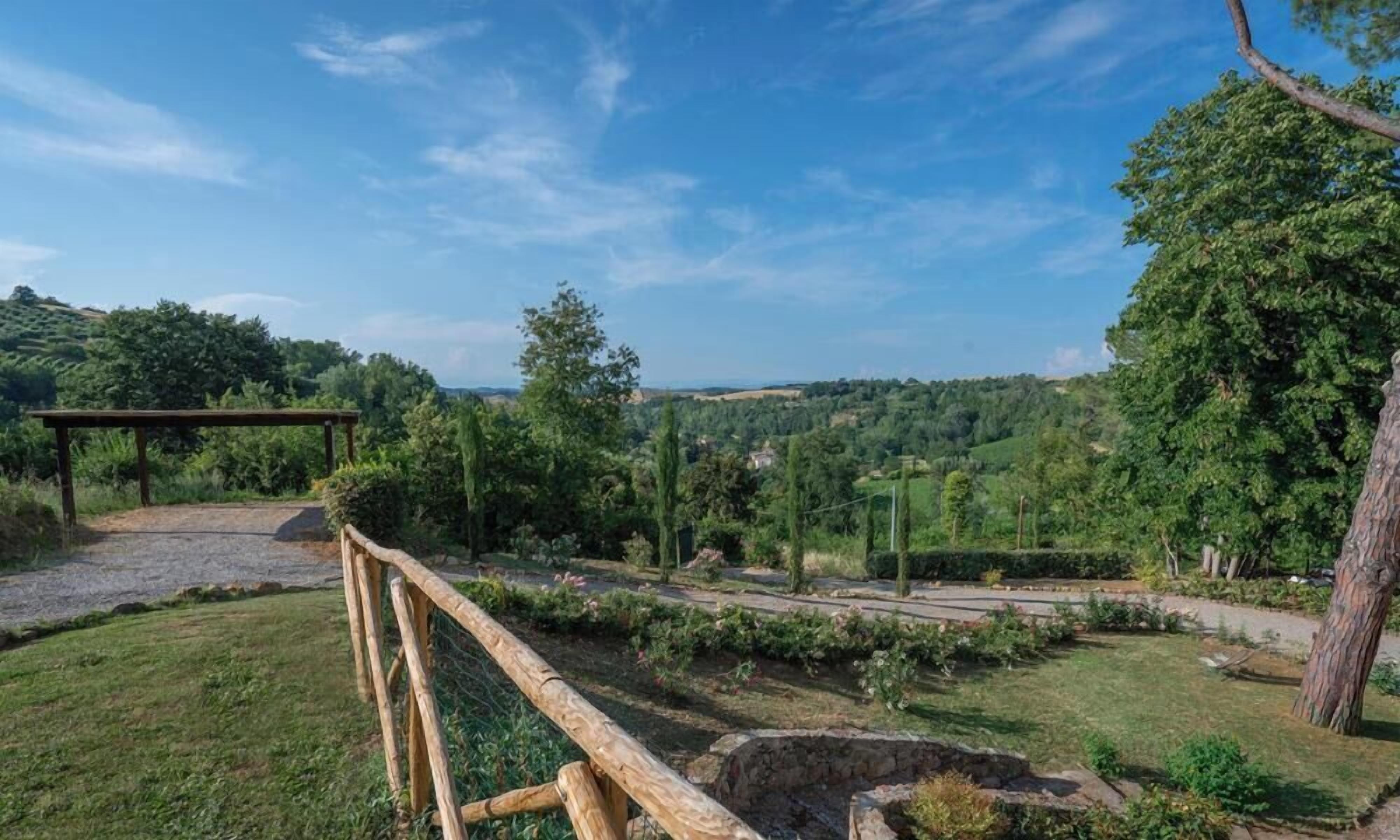 Un espacio exterior cercado con un sendero de grava, un banco de madera y vistas a un paisaje montañoso.
