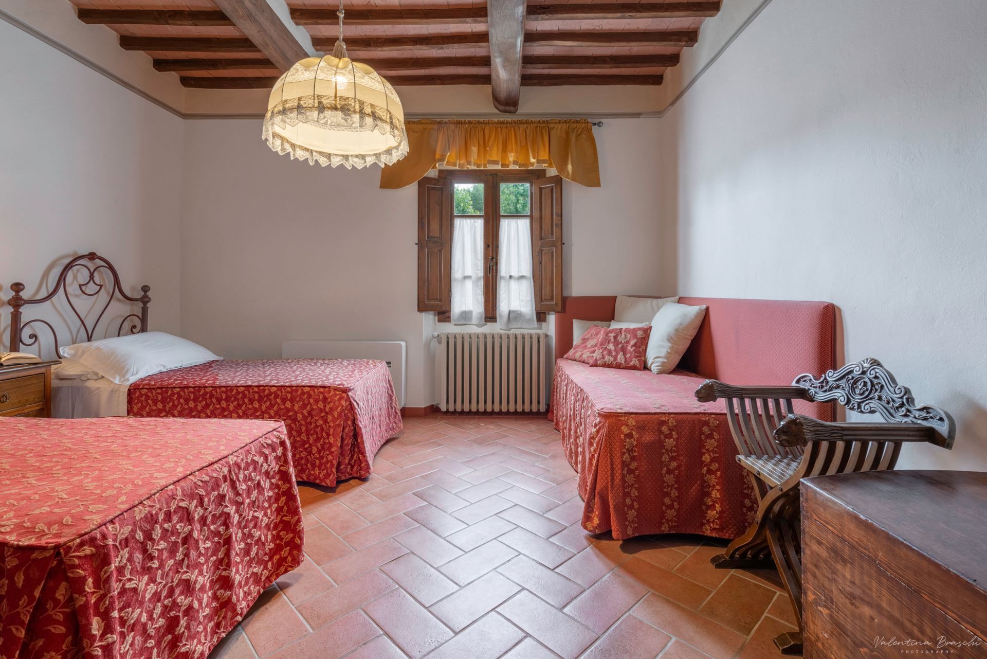 Una stanza con due letti, una panca in legno, un tavolo e un lampadario.