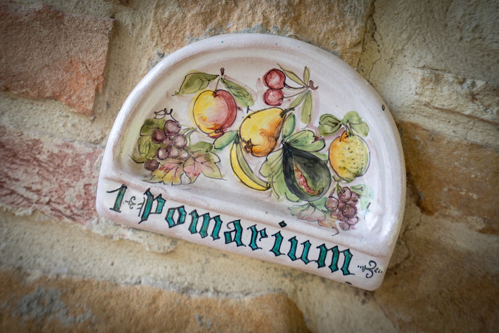 A ceramic wall-mounted sign with fruit illustrations and the text '1 pomarium'.