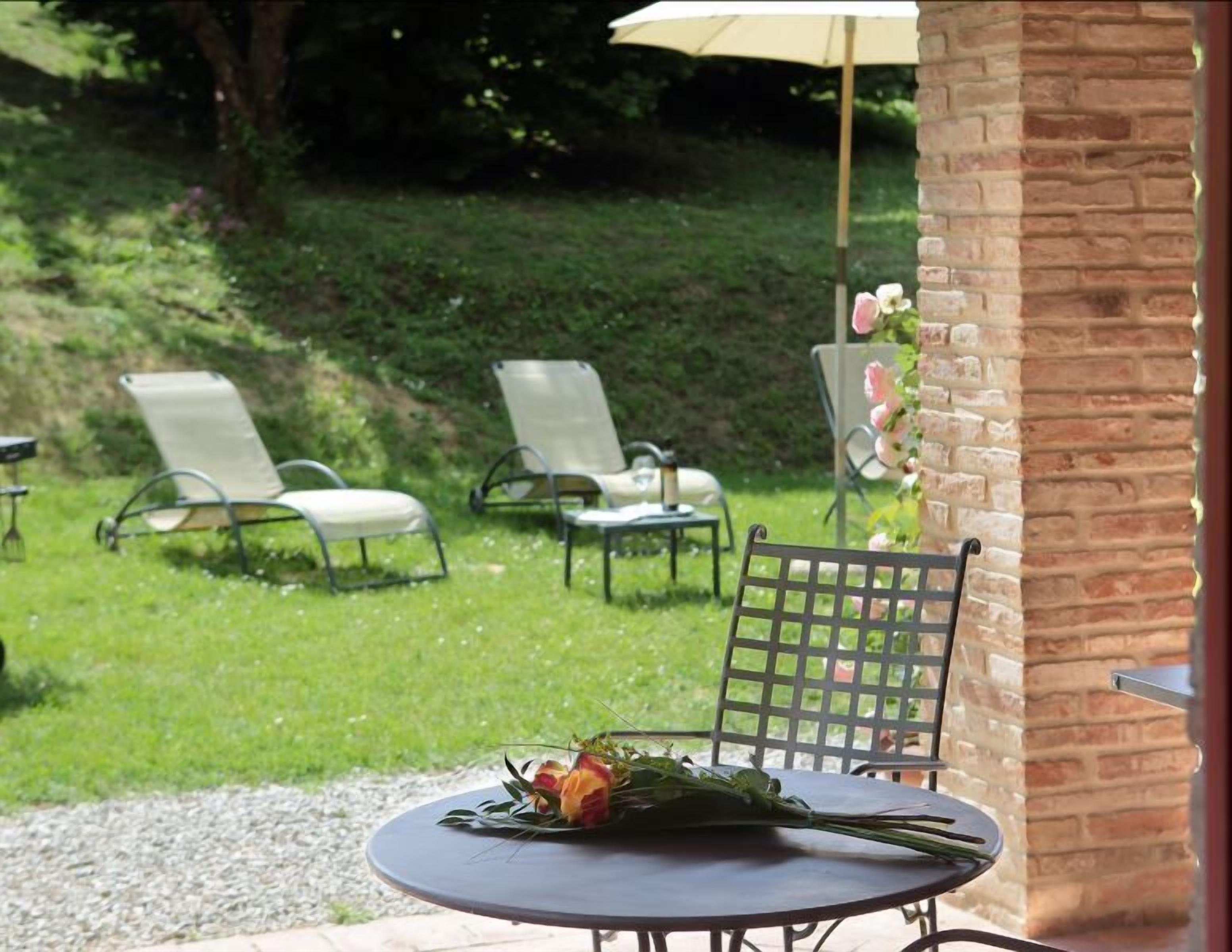 An outdoor seating area with a table and chairs, a brick wall, and a garden view.
