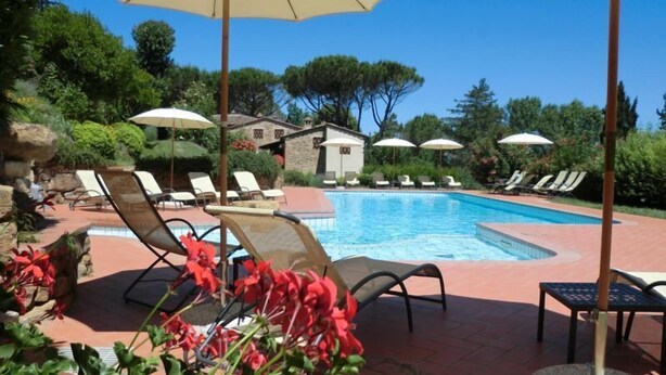 Area piscina con lettini e ombrelloni, immersa nel verde e adiacente a un edificio in pietra.