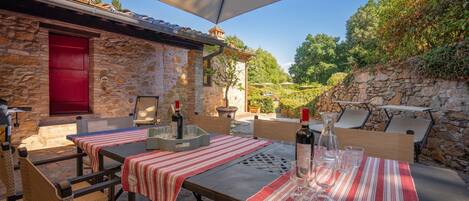 An outdoor dining area with stone walls, red door, and a view of the countryside.