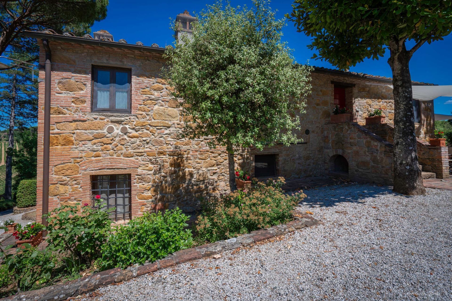A stone building with a gravel driveway, surrounded by greenery and trees.