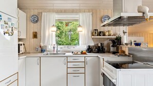Cozinha com armários brancos, janela com cortinas e vista para o verde lá fora.
