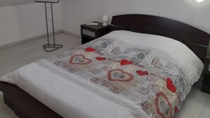 Een slaapkamer met een schuine kap, een bed met een geborduurd sprei, een nachtkastje met een lamp, en een vloerlamp.