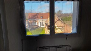 Een kamer met een raam dat uitkijkt over een huis en een tuin.