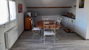 Een compacte keuken met een eethoek, met een houten tafel en metalen stoelen, een koelkast en een magnetron.