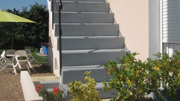 Een trap die leidt naar een gebouw met een beige gevel, een klein raam en een deur met een witte omlijsting.