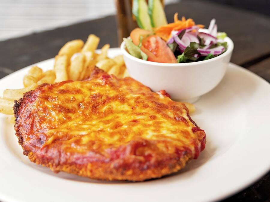 Een bord met een gepaneerde en gebakken schnitzel, frietjes en een salade, met een kop koffie op een tafel.