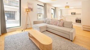 A modern living room with a sectional sofa, a wooden coffee table, and a large window providing natural light. - GuestReady - One prime stay in Campolide (Lisbon)