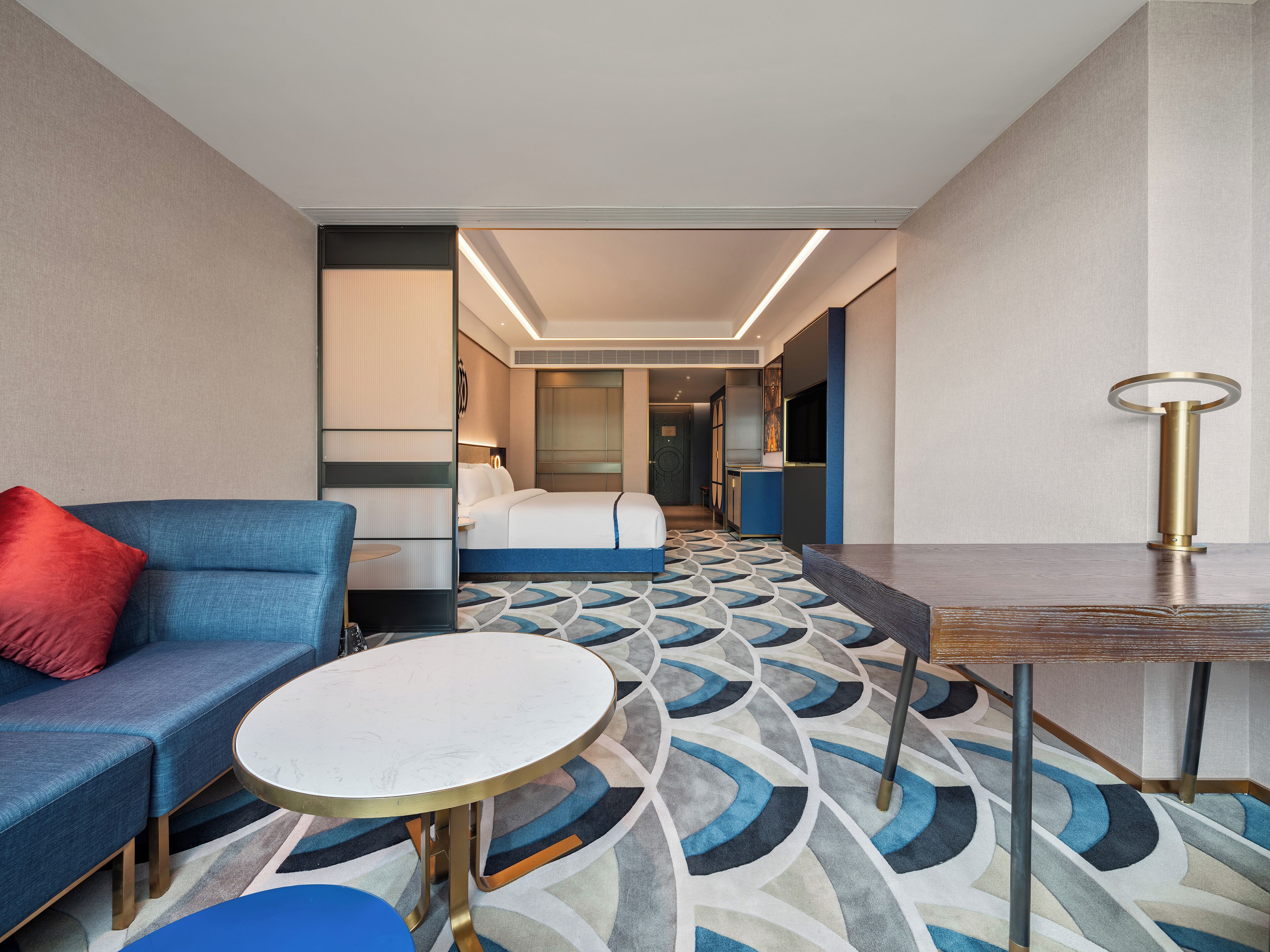 A hotel room with a bed, a blue sofa, a round table, and a patterned carpet.