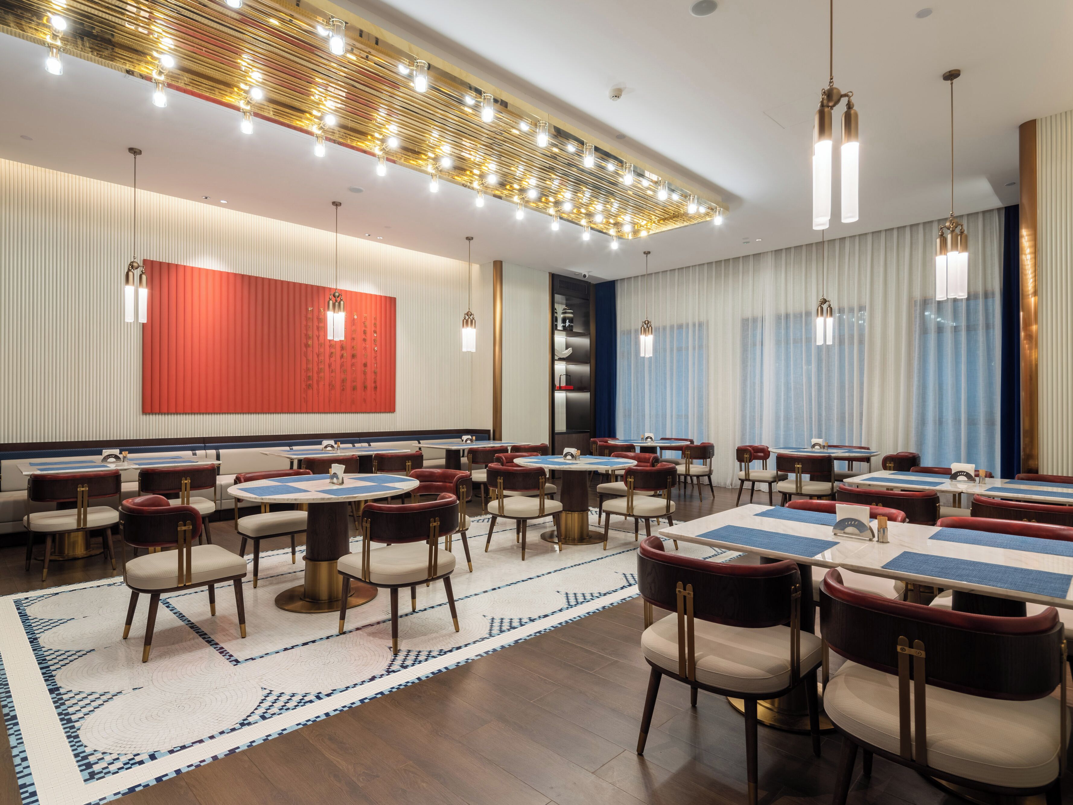 Un vaste espace dédié à la salle à manger, avec plusieurs tables et chaises, un tapis à motifs et un luminaire moderne au plafond.