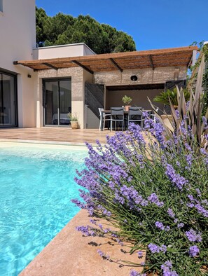 Ein moderner Poolbereich im Freien mit Terrasse, Sitzgelegenheiten und Blick auf einen bewaldeten Hügel.
