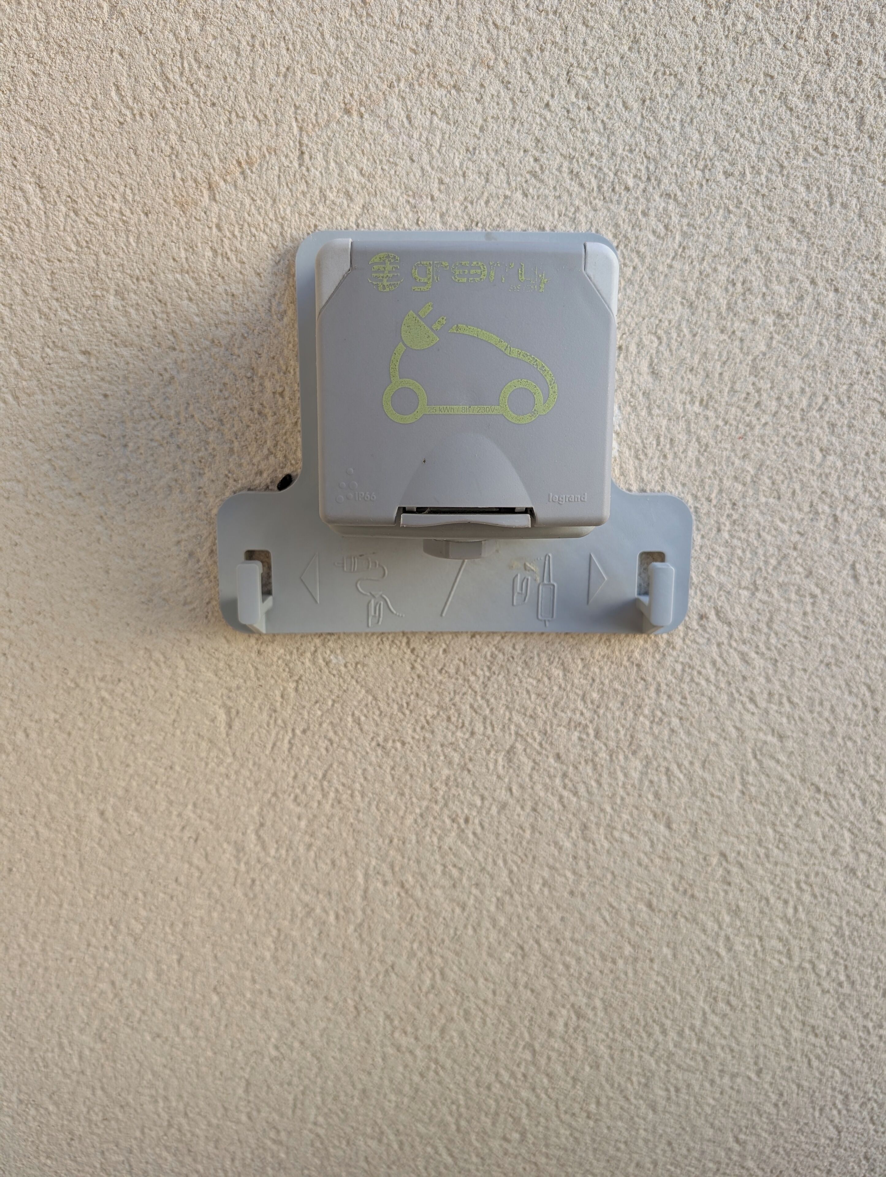 A gray parking meter with a car symbol and a charging symbol, mounted on a textured wall.