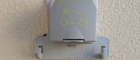 A gray parking meter with a car symbol and a charging symbol, mounted on a textured wall.