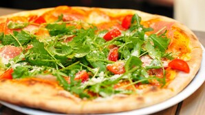 A pizza with fresh greens and tomatoes on a white plate. - Charleville Cattle Camp Hotel  (Charleville)