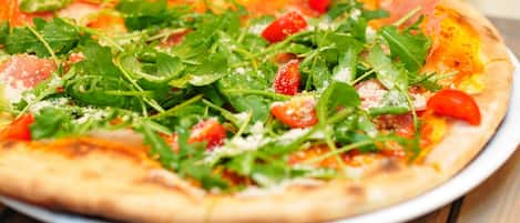 A pizza with fresh greens and tomatoes on a white plate.