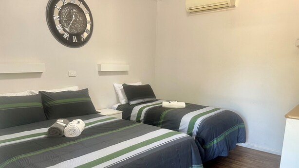 A hotel room with two beds, each with striped bedding and pillows, a wall clock, and an air conditioning unit. - Charleville Cattle Camp Hotel  (Charleville)