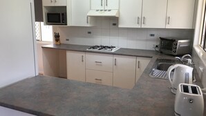 A kitchen with white cabinets, a gas stove, a microwave, a toaster, and a kettle. - Longreach Apartments (Longreach)