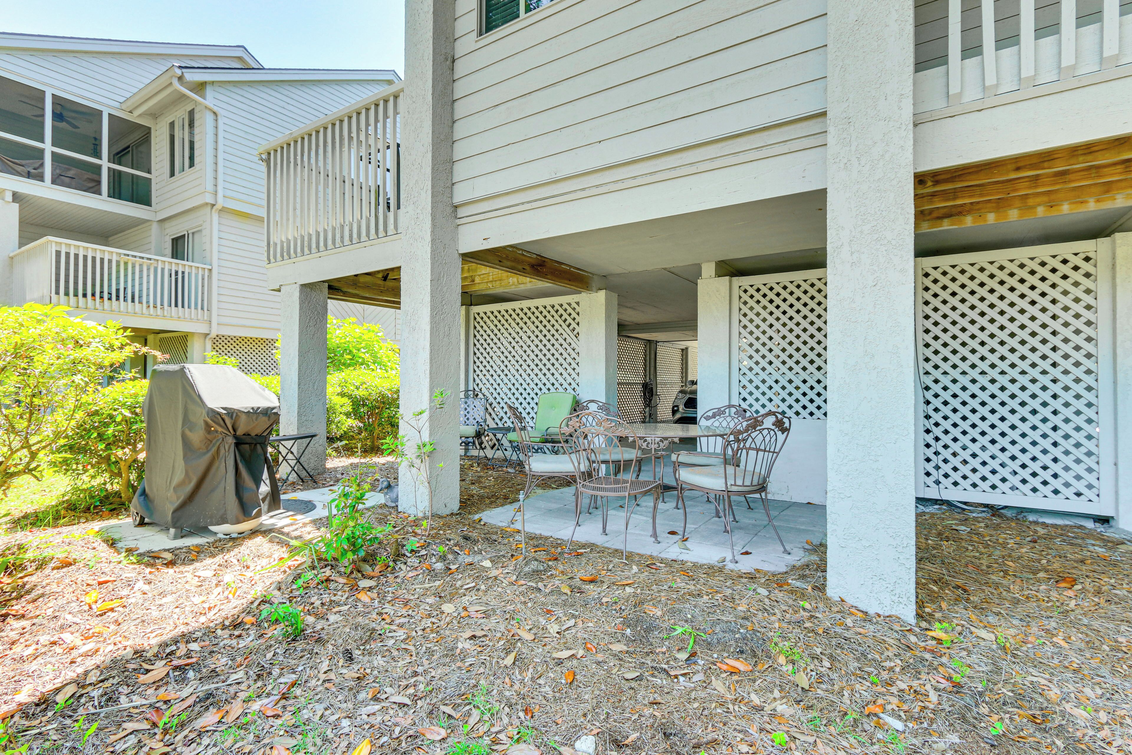 A covered outdoor patio with a grill, chairs, and a table.